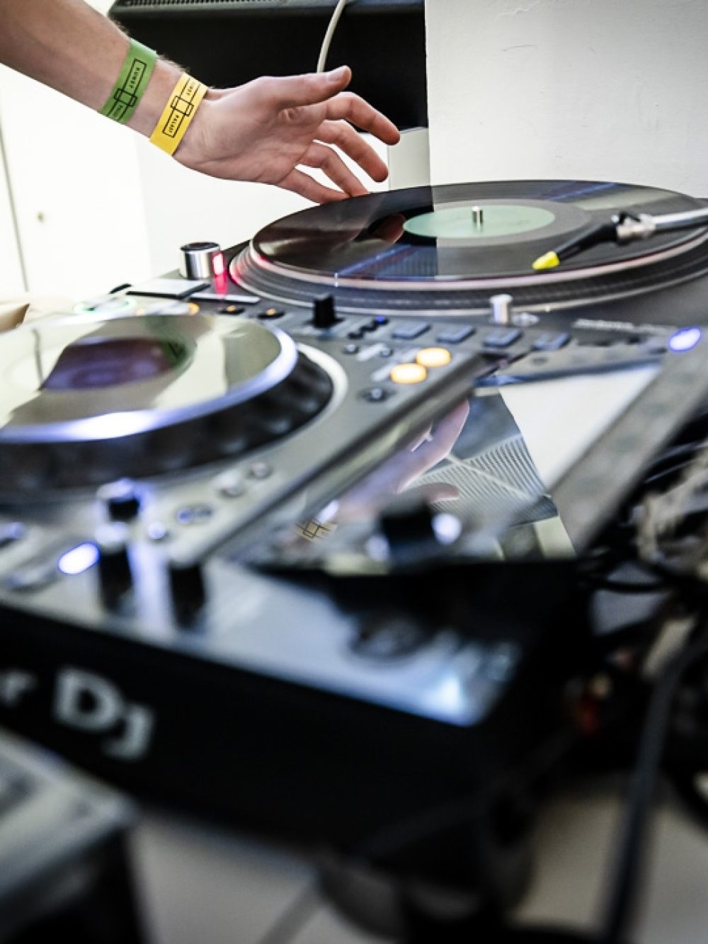 Nahaufnahme eines DJs, der mit der Hand einen Plattenspieler und ein Mischpult einstellt, mit verschiedenen Geräten auf einem Tisch.