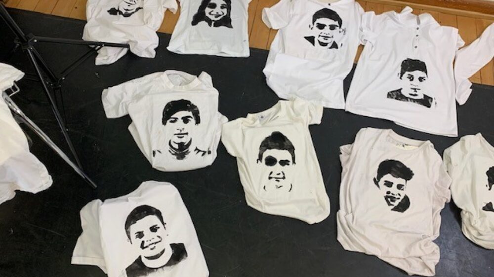 Auf dem Boden liegende, weiße T-Shirts, die in Schwarz mit Gesichtern bedruckt sind