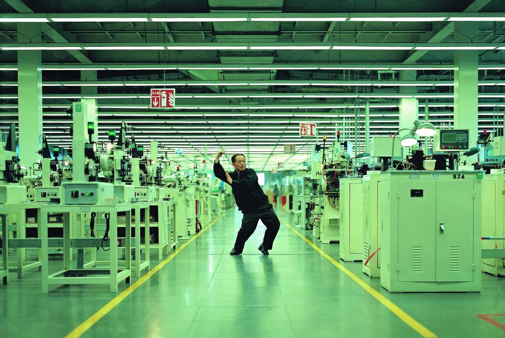 Eine Person posiert energisch inmitten einer hell erleuchteten, modernen Fabrik voller Industriemaschinen.