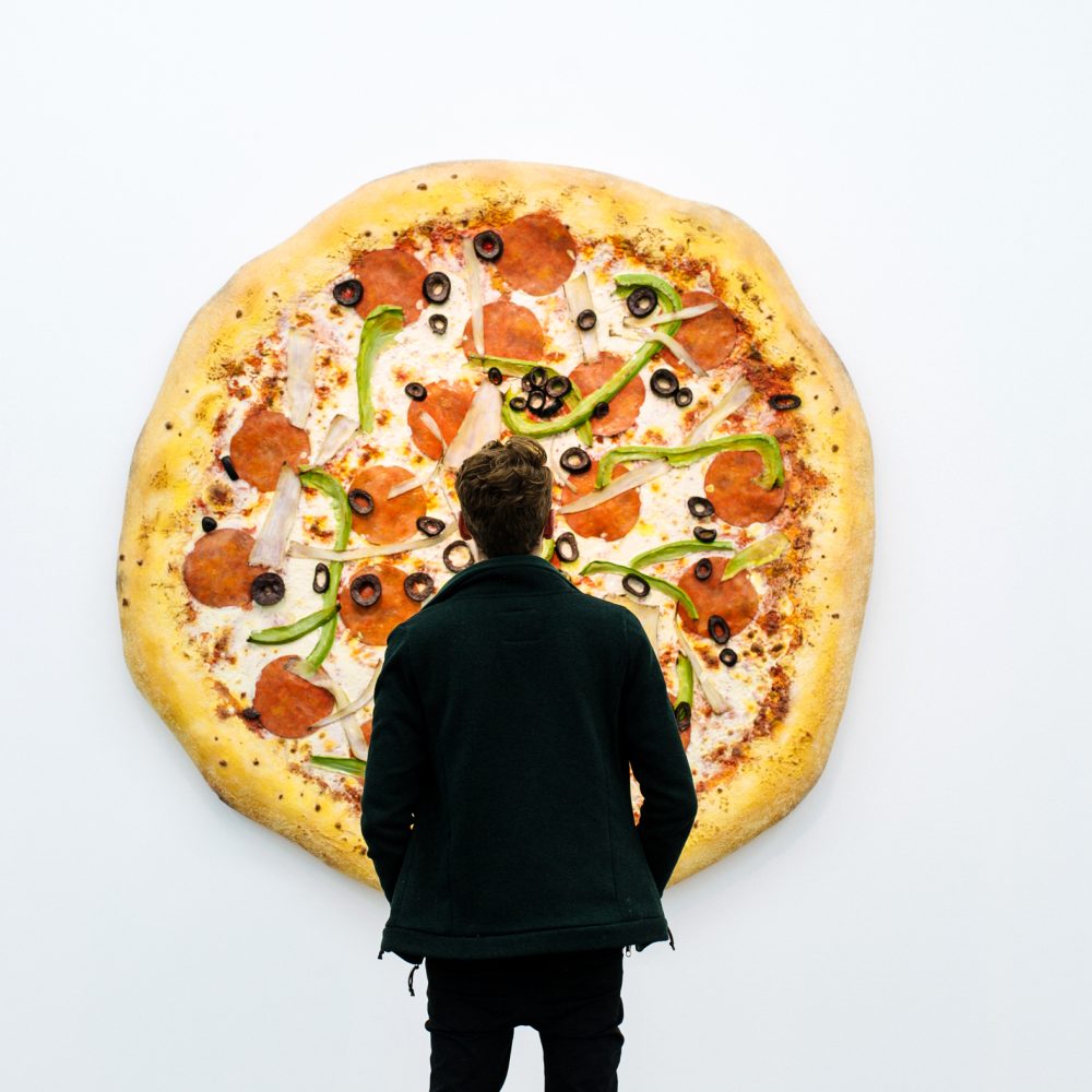 In the exhibition Pizza is God, a man stands in front of an artwork by Tom Friedman, which is a huge pizza hanging on the wall