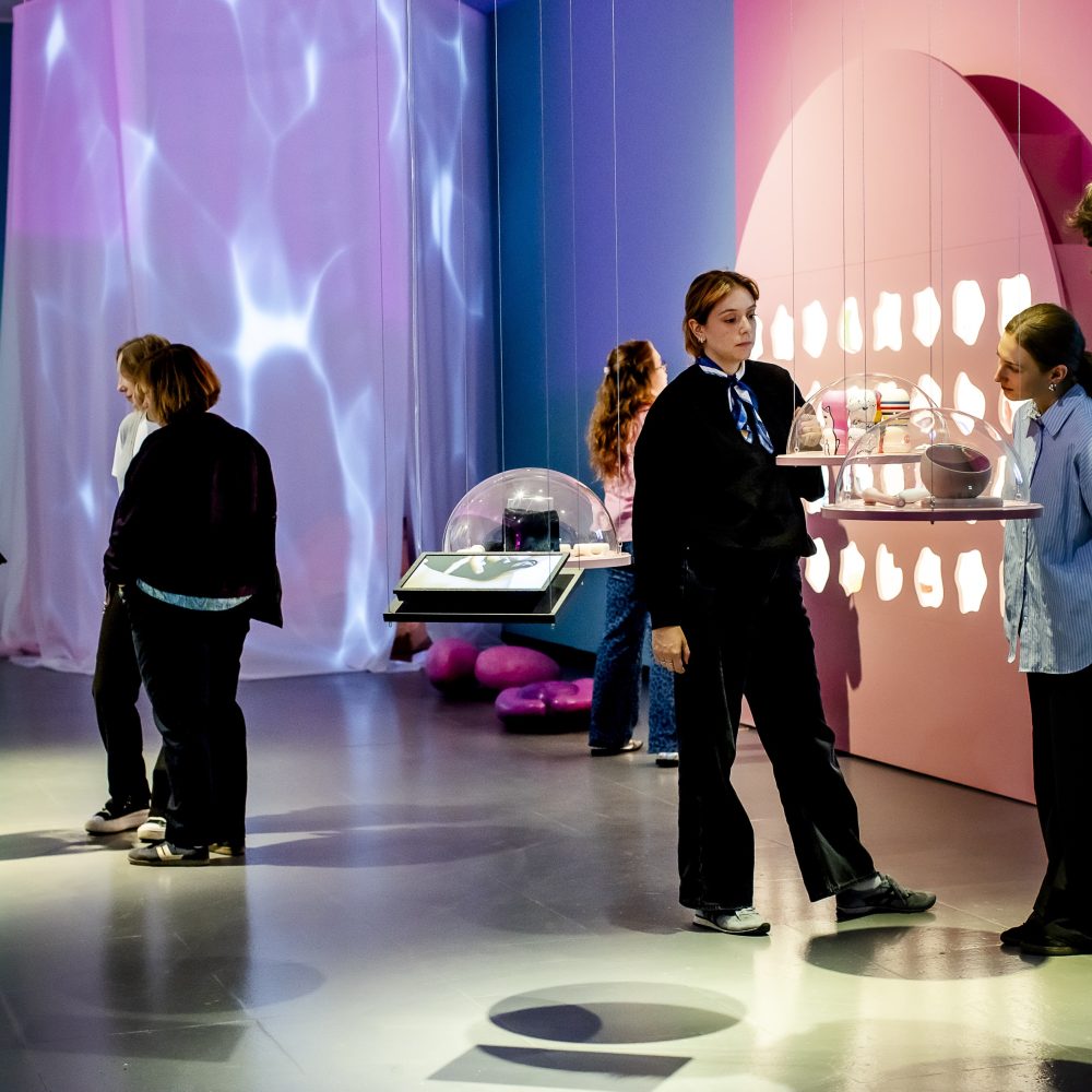 Die Besucher erkunden eine moderne Kunstausstellung mit rosa, blauer und violetter Beleuchtung, interaktiven Displays und futuristischem Dekor.