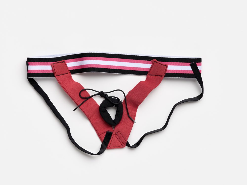 Ein rotes Sportjockstrap mit rosa, weiß und schwarz gestreiftem Bund auf weißem Hintergrund.