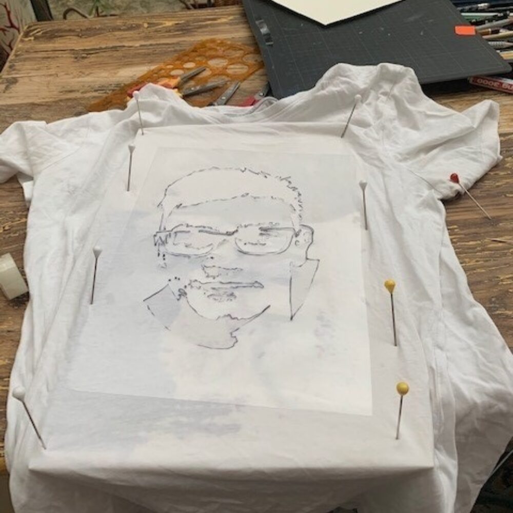 Weißes T-Shirt, dass mit einer Pappe unterlegt ist und auf dem die Konturen eines Gesichts eines Jugendlichen abgezeichnet sind