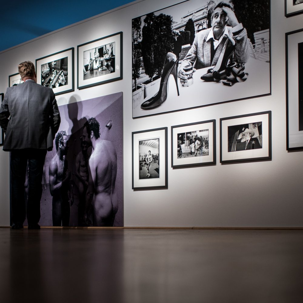 Mann in der Ausstellung 100 Jahre Nikon vor einer Wand an der mehrere gerahmte Fotografien hängen