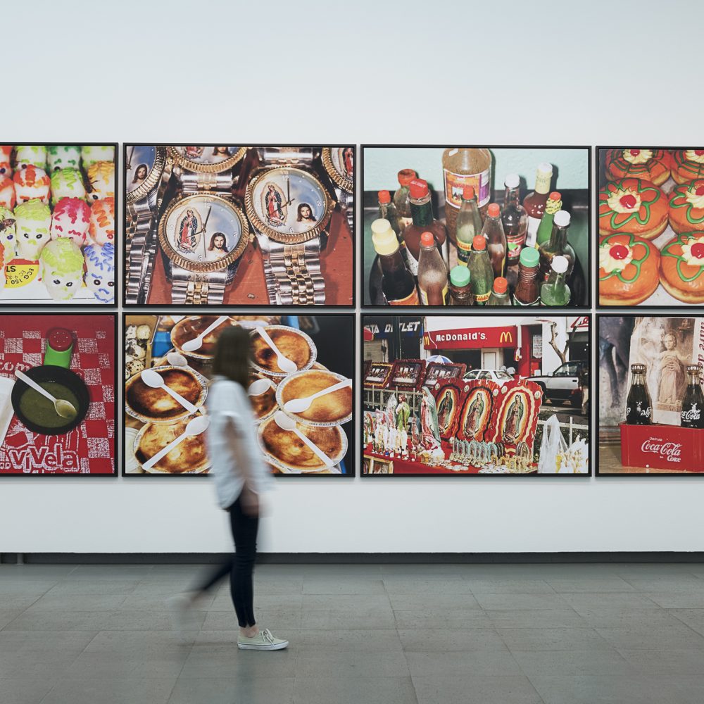 Eine Person läuft in der Martin Parr Retrospektive an einer Wand an der Bilder von Martin Parr hängen vorbei