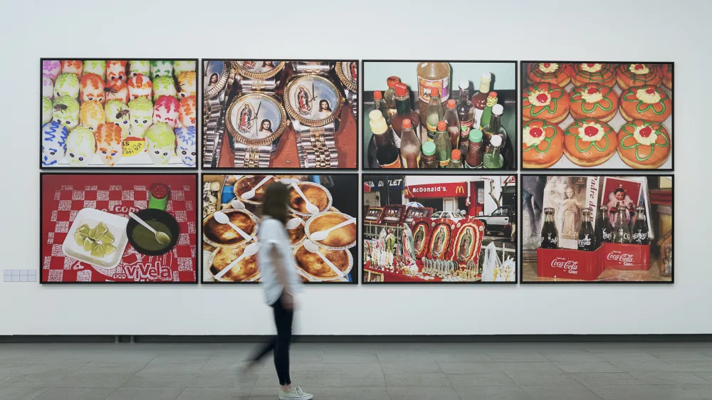 In the Martin Parr retrospective, a person walks past a wall with pictures by Martin parr hanging on it