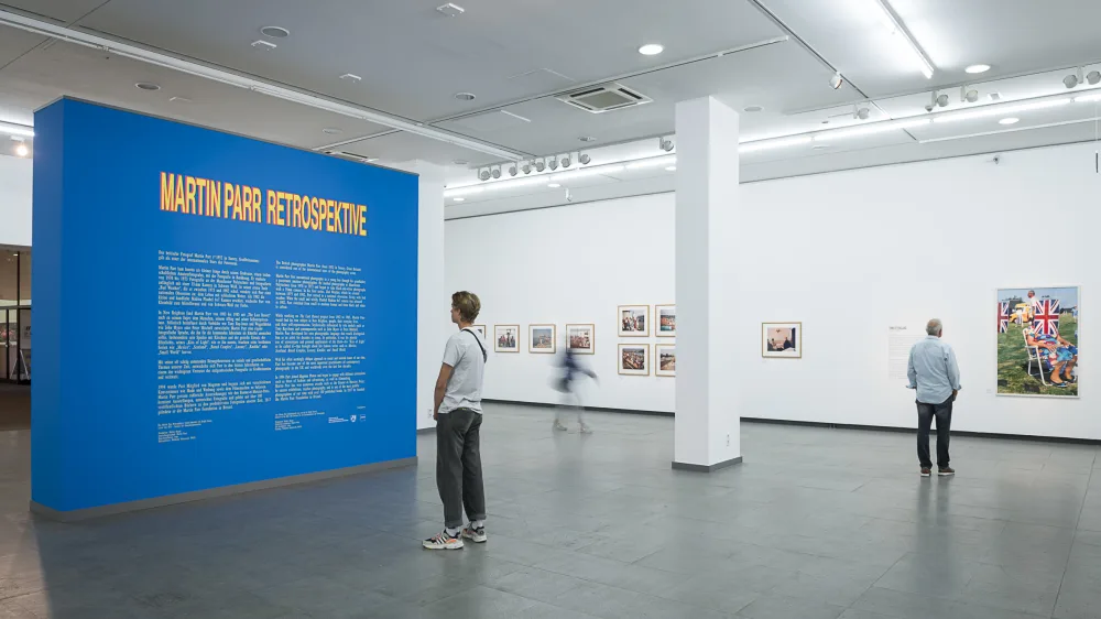 Several people are in the Martin Parr retrospective and enjoy the exhibition
