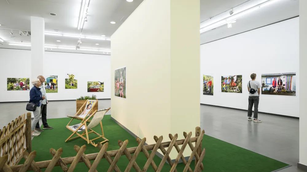 Several people stand in the Martin Parr retrospective and look at photographs