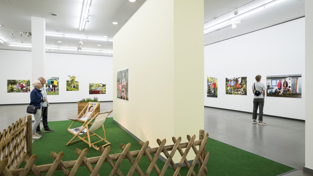 Several people stand in the Martin Parr retrospective and look at photographs