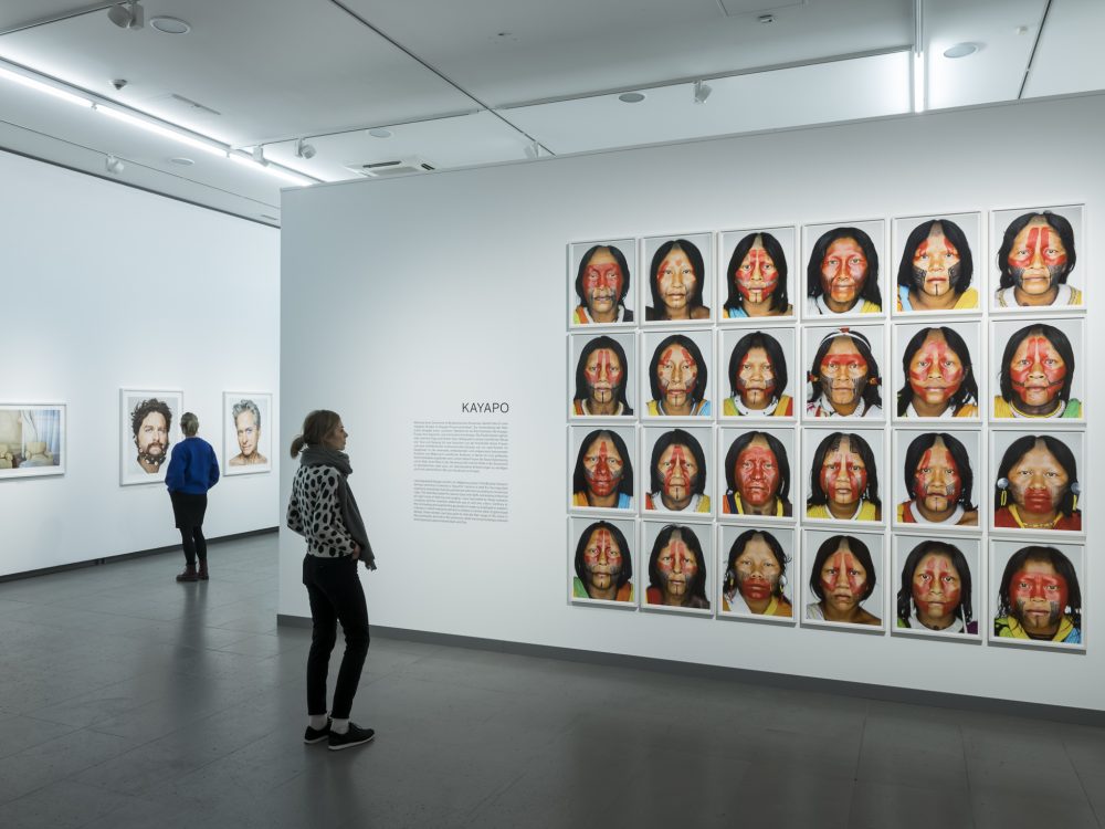 Ausstellungsansicht der Serie Kayapo aus der Ausstellung Martin Schoeller mit mehreren gleichgestalteten Porträts von indigenen Frauen in Blockhängung