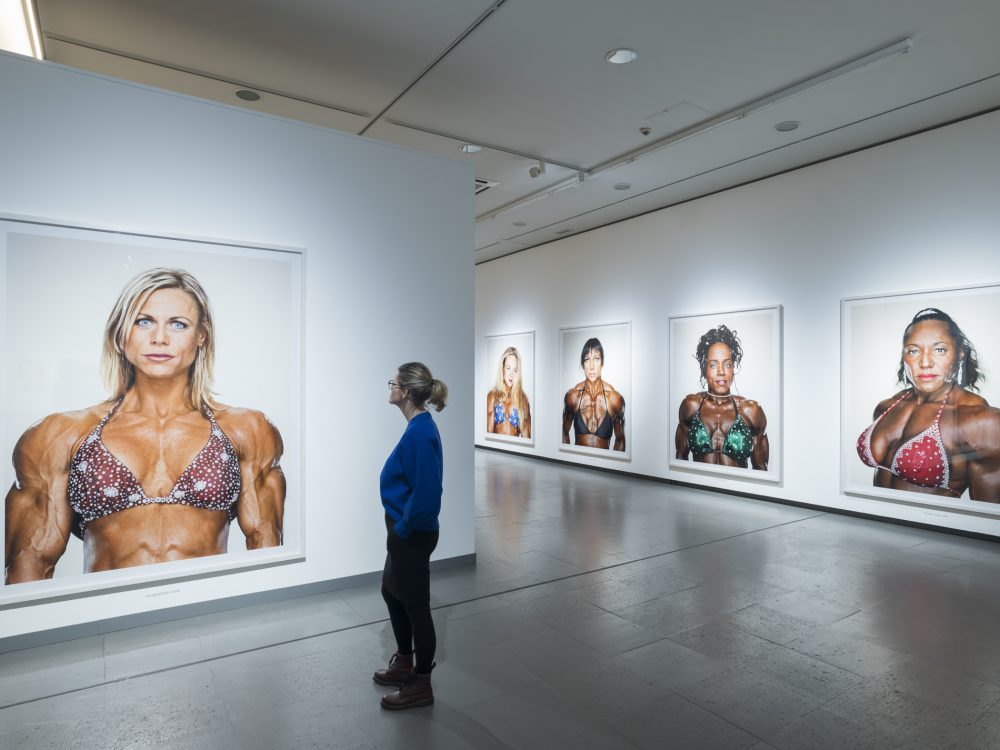 Eine Frau betrachtet Fotos von weiblichen Bodybuilderinnen in der Ausstellung Martin Schoeller