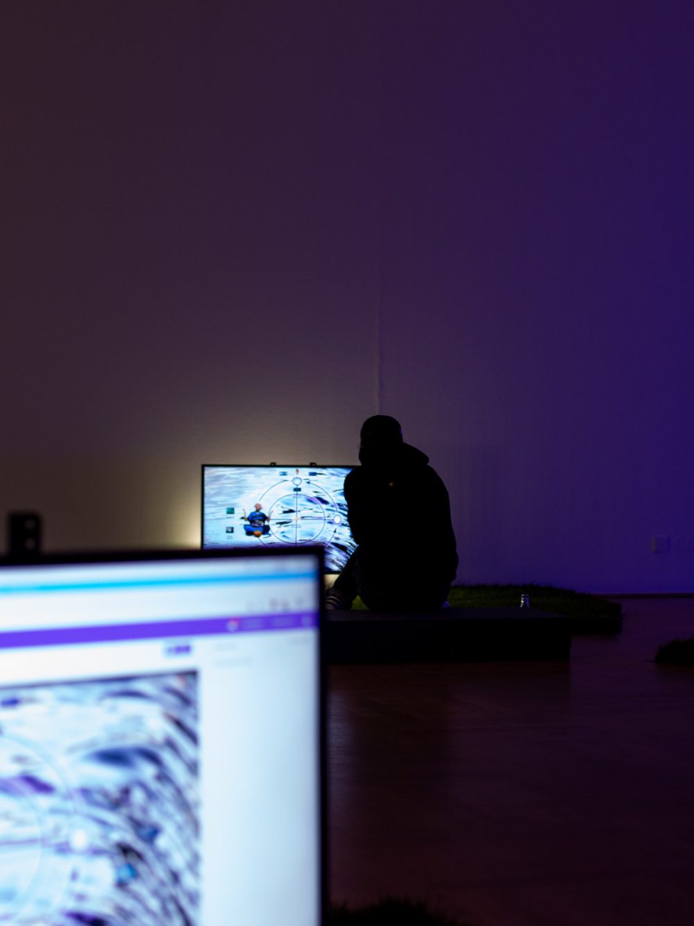Eine Person sitzt in einem dunklen Raum mit hellen Monitoren