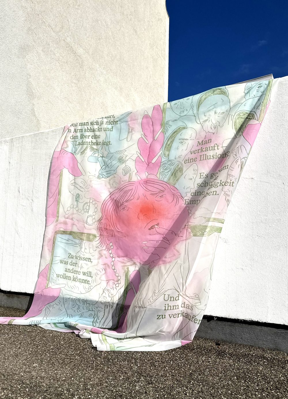 Ein durchsichtiges Tuch mit pastellfarbenen Zeichnungen und deutschem Text, drapiert an einer weißen Wand im Freien, unter einem klaren blauen Himmel.