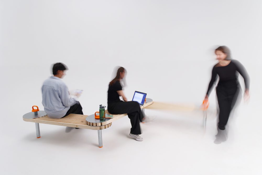 Unscharfes Bild von drei Personen auf einer Bank in einem Studio. Zwei sitzen, eine steht und bewegt sich.