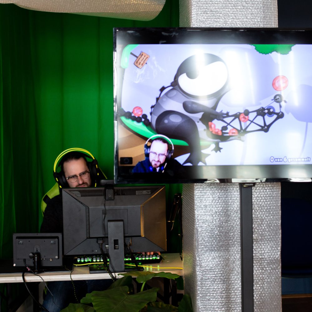 Ein Mann sitzt hinter einem Computerbildschirm und streamt sich, was auf einem Bildschirm davor übertragen wird