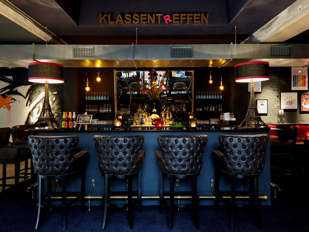Hotelbar in dunklen Braun und Blautönen mit schwarzen Lederhockern in gedämpftem Licht