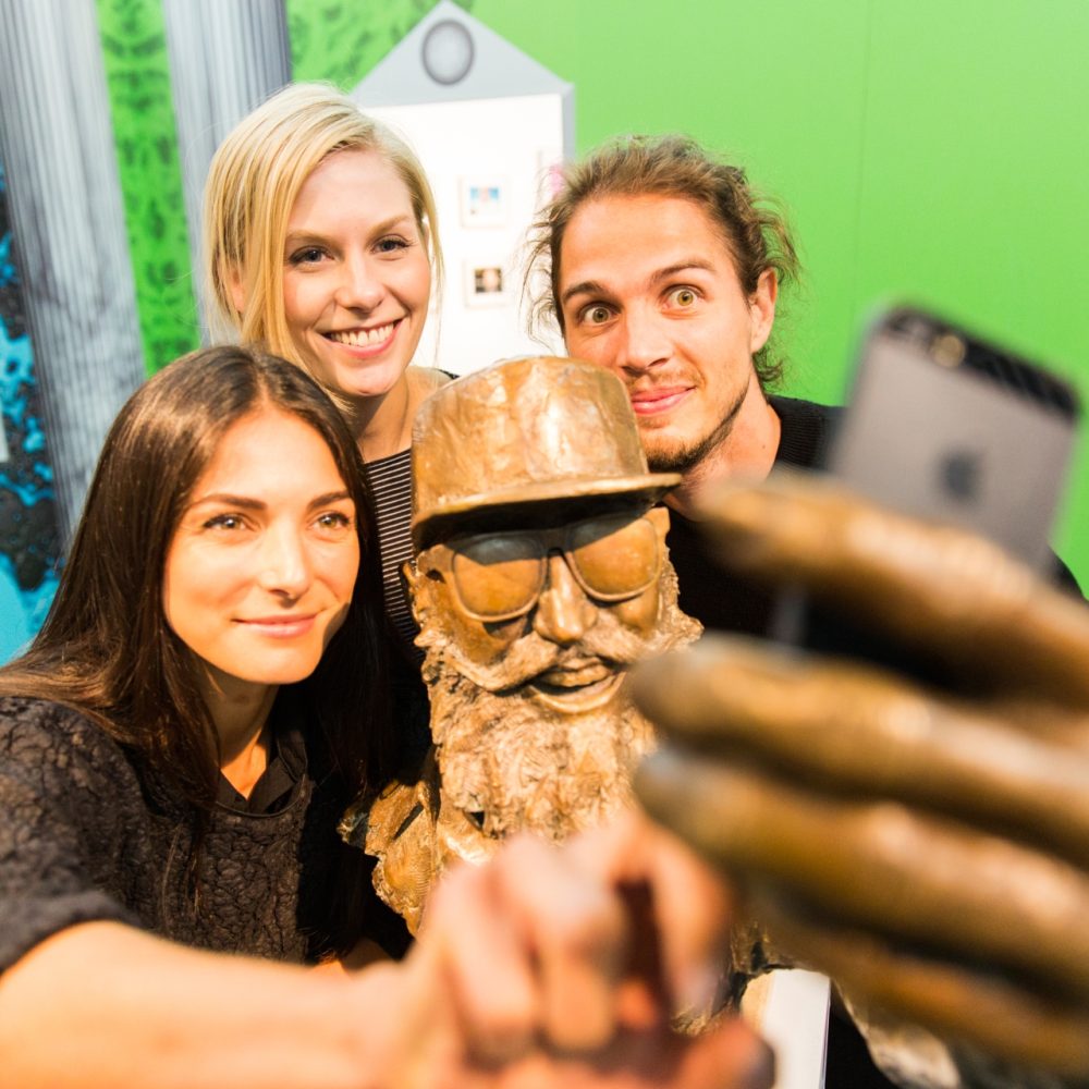 Drei Personen machen ein Selfie mit einer Büste des Musikers MC Fitti