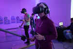 Ältere Frau steht in lila beleuchtetem Raum und hat VR Brille auf dem Kopf sowie einen Controller und ein elektronisches Schwert in der Hand