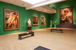 Grün gestrichener Ausstellungsraum mit alten Gemälden, Skulpturen und Sitzgelegenheiten