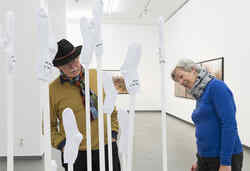 Ein älterer Mann und eine ältere Frau schauen sich in der Ausstellung gute Aussichten ein Kunstwerk an bei dem weiße Socken auf Stäbe gesteckt sind