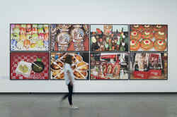 In the Martin Parr retrospective, a person walks past a wall with pictures by Martin parr hanging on it