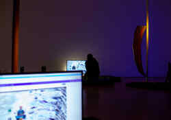 Eine Person sitzt in einem dunklen Raum mit hellen Monitoren