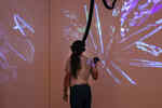 Woman standing in the Pendoran Vinci exhibition with VR glasses on her head and a controller in her hand, illuminated by projectors