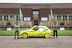 A yellow car in which a man is sitting stands in front of the NRW Forum. On the car it says: Talk to me. I will drive you