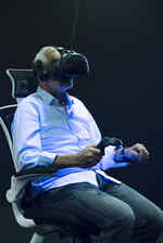 Ein älterer Mann sitzt auf einem Drehstuhl in der Ausstellung Whiteout mit einer VR Brille auf dem Kopf und wird von Schwarzlich beleuchtet
