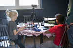 Two children sit at a table with a laptop with an open game, Lego bricks and a tripod with a camera
