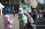 Die Maskottchen des NRW Forums Data und Zip umarmen in der Düsseldorfer Innenstadt einen älteren Mann