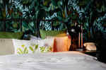 hotel bed with green and white sheets and pillow with flower motif in front of wall with photo wallpaper with jungle image