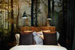 Hotelbett mit weißer und brauner Bettwäsche und Hasenkissen mit Kopfteil aus Holz auf dem zwei Lampen stehen vor Wand mit Fototapete mit Waldmotiv