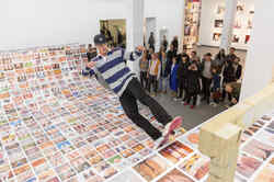 Ausstellungsansicht der Ausstellung Ego Update mit einer mit Fotos beklebten Skateramp auf der ein Skater fährt, während er von Leuten beobachtet wird