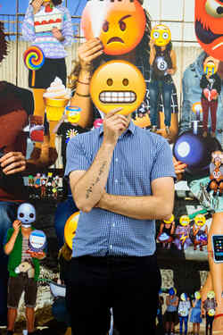 Alain Bieber, künstlerischer Leiter des NRW Forums, hält sich ein auf Pappe gedrucktes Emoji, dass seine Zähne zeigt, vor sein Gesicht
