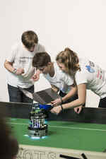 Jugendliche mit Laptop in der Hand programmieren einen Roboter, der auf einem grünen Spielfeld steht