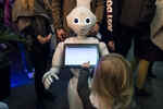 Kind bedient bei einer Veranstaltung mit vielen Leuten im Hintergrund einen weißen Roboter mit Touchscreen