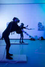 Two people play in a blue-lit room with VR glasses on their heads and controllers in their hands